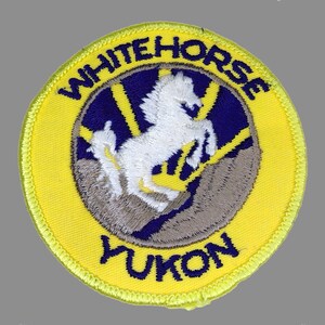 May include: Yellow embroidered patch with a white horse running up a mountain, with the words "Whitehorse Yukon" around the edge.