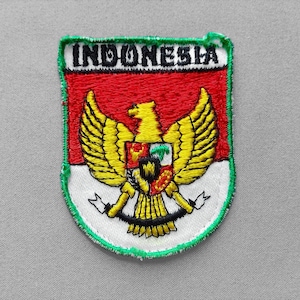 May include: An embroidered patch featuring the Indonesian coat of arms, the Garuda, in yellow with a red and white background. The word INDONESIA is stitched in black at the top. The shield on the bird's chest displays various symbols in red, white, black, and green.