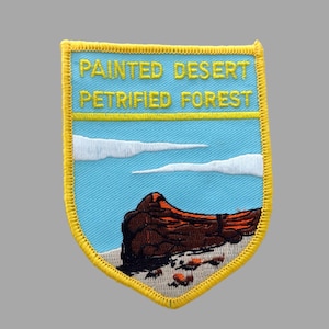 May include: Embroidered patch featuring a landscape scene with the text "PAINTED DESERT PETRIFIED FOREST". The patch has a blue background with white clouds, a brown rock formation, and a yellow border.