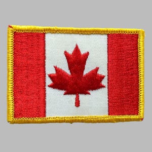 May include: Embroidered patch featuring the Canadian flag. The design includes a red maple leaf centered on a white background, flanked by red vertical stripes. The patch has a yellow border.