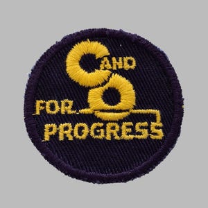 May include: Embroidered patch with a navy blue background and a yellow design. The patch reads "C and O FOR PROGRESS" in yellow, stylized lettering. The patch is circular with a dark purple border.