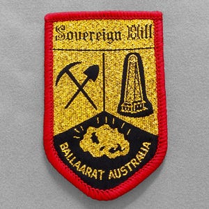May include: Embroidered patch with a red border and a gold and black design. The patch features the text "Sovereign Hill" at the top, with crossed pickaxe and shovel, a tower, and the words "BALLAARAT AUSTRALIA".