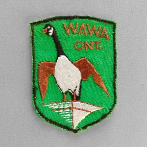 May include: Embroidered patch featuring a goose with outstretched wings, set against a green shield. The patch includes the text "WAWA ONE" in orange. The goose has a white body, brown wings, and a black neck.