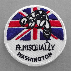 May include: White embroidered patch with a black silhouette of a bee on a red, white, and blue Union Jack flag. The text "R. Nisqually Washington" is written in black below the flag.