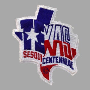 May include: Embroidered patch in the shape of Texas, featuring a blue and white star and the text "TEXAS" in white. The word "SESQUICENTENNIAL" is in red and white. The patch has a white border and a gray background.