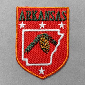 May include: Embroidered red patch featuring the word "ARKANSAS" in green, white stars, and a white outline of the state with a pine cone and branch. The patch has an orange border.