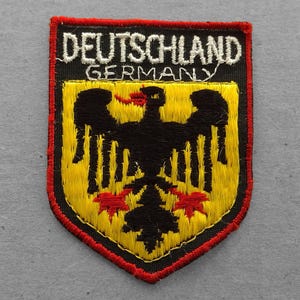 May include: A black and yellow embroidered patch with the text "DEUTSCHLAND GERMANY" and a black eagle with red accents.