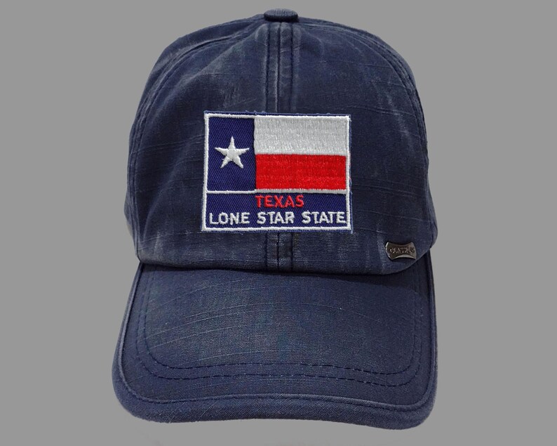 May include: A dark blue baseball cap with a distressed look. The front of the cap features an embroidered patch with the Texas flag and the text "Texas Lone Star State".