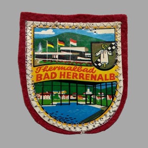May include: A vintage patch with a shield shape, featuring a colorful illustration of a building with flags, a lake, and the text "Thermalbad BAD HERRENALB." The patch has a red border and a stitched edge.