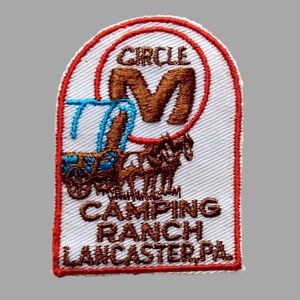 May include: Embroidered patch with a white background and a red border. The patch features the text "CIRCLE M CAMPING RANCH LANCASTER PA" and an illustration of a horse-drawn carriage. The letter "M" is prominently displayed.