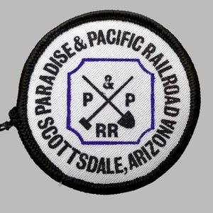 May include: A round patch with the text "SCOTTSDALE & PARADISE & PACIFIC RAILROAD ARIZONA" in a circular pattern. The center features a blue and white design with crossed tools and the letters "P & P RR". The patch has a black border.