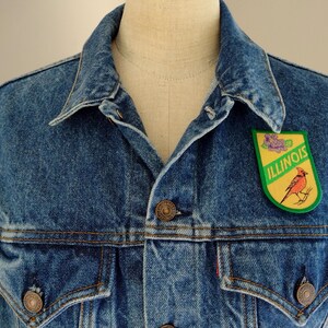 May include: A blue denim jacket with a green and yellow patch featuring a cardinal bird and the word "ILLINOIS".