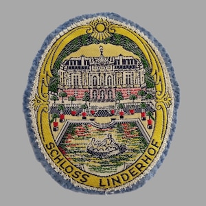 May include: Oval patch with a detailed embroidered image of Schloss Linderhof, a Bavarian palace. The palace is depicted in the center, surrounded by a yellow and green border, with the words "SCHLOSS LINDERHOF" in yellow. The patch has a blue border.