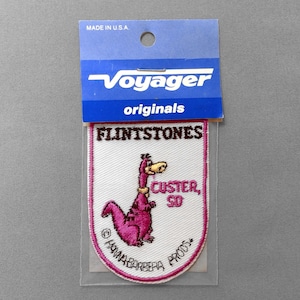 May include: A vintage patch featuring a pink cartoon dinosaur from The Flintstones, with the text "FLINTSTONES" and "CUSTER, SD." The patch is bordered in pink and includes the text "Hanna-Barbera Prods."