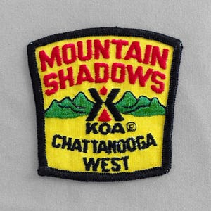 May include: Yellow and black embroidered patch with the text "Mountain Shadows KOA Chattanooga West". The patch features a stylized tent and mountains.