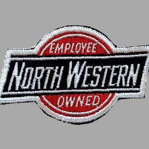 May include: Embroidered patch with the words "EMPLOYEE" and "OWNED" in a red oval, and "NORTH WESTERN" in a black rectangle. The patch has a white border and is likely for a uniform or apparel.