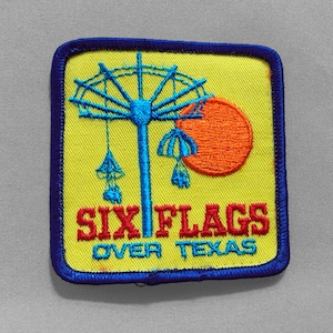 May include: Embroidered patch featuring a Ferris wheel design with an orange sun on a yellow background. The text "SIX FLAGS OVER TEXAS" is in red and teal. The patch has a blue border.