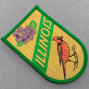 May include: A yellow and green embroidered patch with the word "ILLINOIS" in green letters and a purple flower and a red bird on a branch.