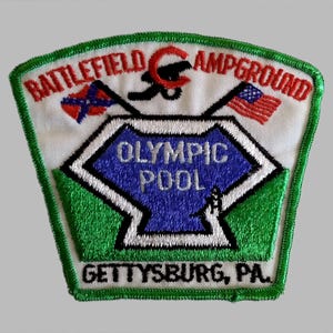 May include: Embroidered patch with a white background, green border, and text that reads "Battlefield Campground" and "Gettysburg, PA." The patch features a blue and white geometric shape with the words "Olympic Pool" and two flags.