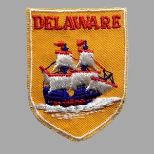 May include: A yellow embroidered patch with the word "DELAWARE" in red lettering and a white and blue ship with red sails.