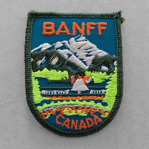 May include: A green, blue, and white embroidered patch with the text "BANFF CANADA" and a mountain scene.