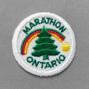 May include: Embroidered patch with the words "MARATHON ONTARIO" in green. A green tree, rainbow, and yellow basket are in the center. The patch is round with a white border.