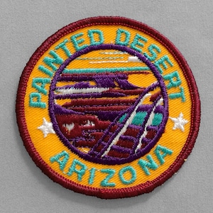 May include: Embroidered patch with the words "Painted Desert Arizona" in teal lettering on a yellow background. The patch features a landscape design with purple, red, and teal elements, and two white stars.