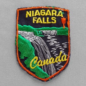 May include: Embroidered patch featuring Niagara Falls, with the text "NIAGARA FALLS" in yellow above a waterfall illustration. The word "Canada" is in yellow script at the bottom. The patch has a black background with green and orange accents.