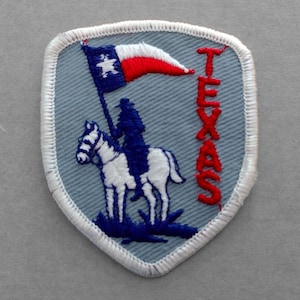 May include: A blue and white embroidered patch with a white horse and rider, a red and white Texas flag, and the word "TEXAS" in red lettering.