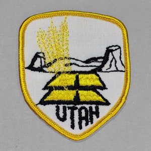 May include: Yellow and black embroidered patch with a stylized wheat stalk design and the word "UTAH" in black lettering.