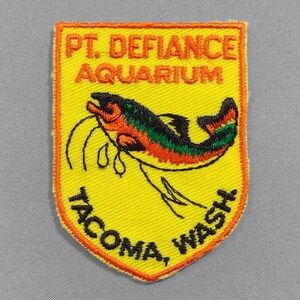 May include: Embroidered yellow patch with orange border. Features a colorful fish illustration and text: "PT. DEFIANCE AQUARIUM TACOMA, WASH."