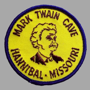 May include: Embroidered patch featuring a portrait of Mark Twain, with text reading "Mark Twain Cave Hannibal Missouri." The patch has a yellow background, a blue border, and brown text and portrait details.