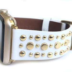 以下が含まれることがあります： ゴールドスタッズが付いた白い革製のApple Watchバンド