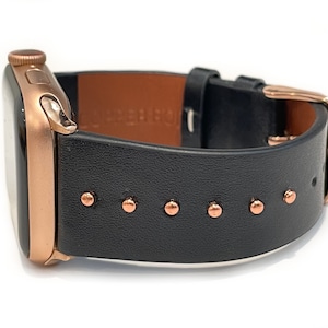 May include: A rose gold Apple Watch with a black leather band featuring copper-colored studs.