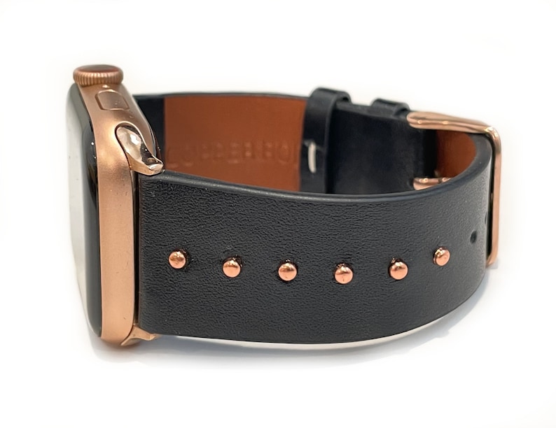 May include: A rose gold Apple Watch with a black leather band featuring copper-colored studs.