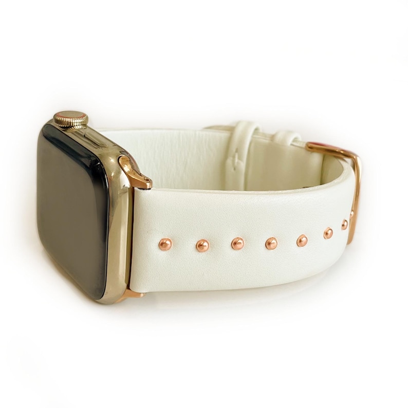 May include: White leather Apple Watch band with rose gold accents and studs.