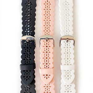 May include: Three silicone watch bands with a floral cut-out design. The bands are black, pink, and white.