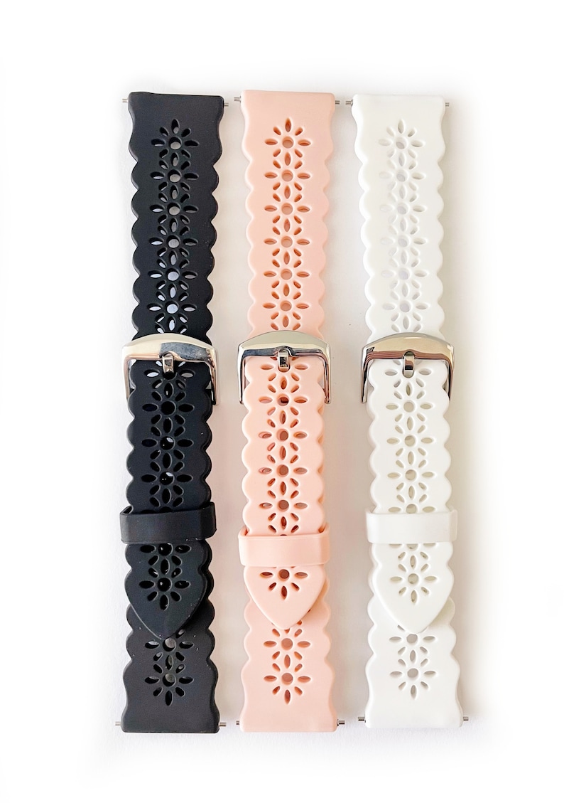 May include: Three silicone watch bands with a floral cut-out design. The bands are black, pink, and white.