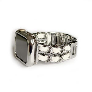 May include: A silver-toned smartwatch case with a matching metallic link bracelet. The bracelet features two parallel rows of silver-coloured metal chains interwoven with white leather strips, creating a textured, multi-strand design.