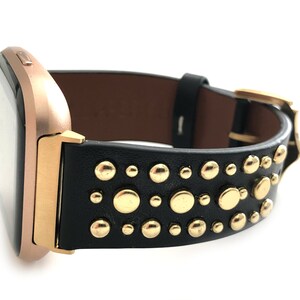 May include: A black leather watch band with gold studs. The band is designed for a square-shaped smartwatch.