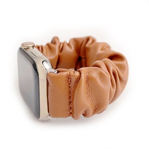 Op de afbeelding: Een bruinleren scrunchie horlogeband. De band is gemaakt van geplooid leer en is bevestigd aan een zilverkleurige horlogekast. De horlogeband is ontworpen voor een smartwatch en heeft een casual, stijlvolle uitstraling.