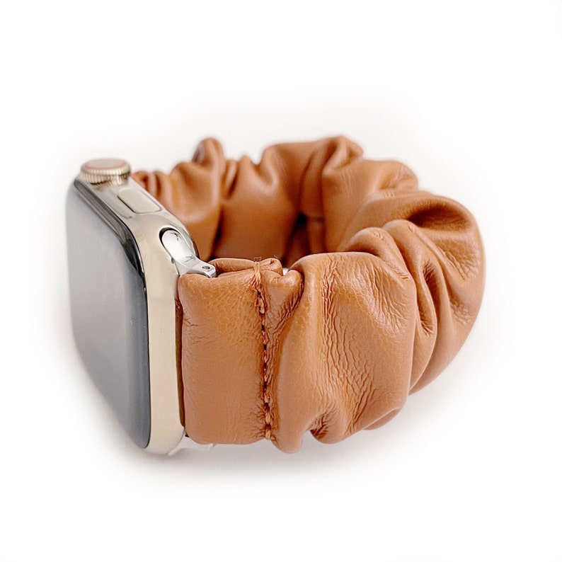 Op de afbeelding: Een bruinleren scrunchie horlogeband. De band is gemaakt van geplooid leer en is bevestigd aan een zilverkleurige horlogekast. De horlogeband is ontworpen voor een smartwatch en heeft een casual, stijlvolle uitstraling.