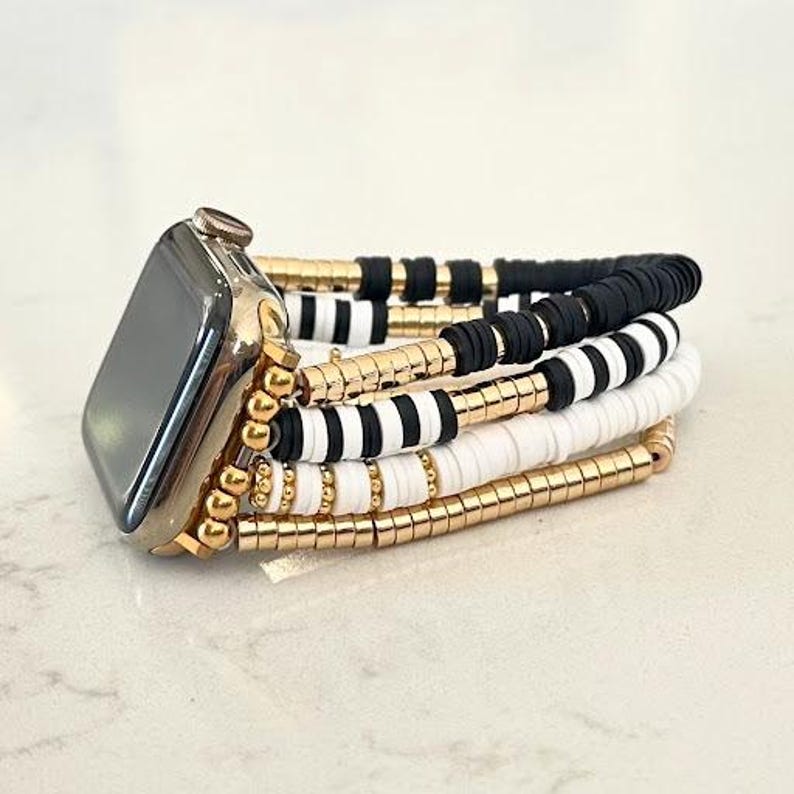 May include: A black and white beaded Apple Watch band with gold accents. The band is made of multiple layers of beads, including black and white striped beads, white beads, and gold beads.