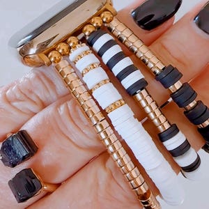 May include: A gold watch band with multiple black and white beaded bracelets attached. The bracelets are made of small round beads and flat, rectangular beads.