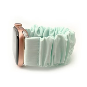 May include: A rose gold Apple Watch with a light blue, gathered fabric band.