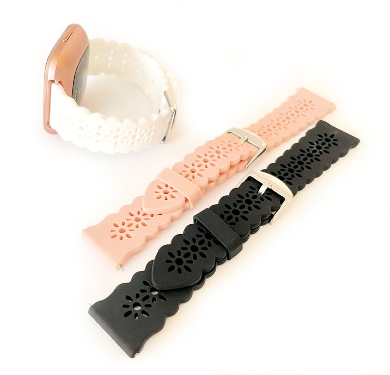 May include: Three silicone watch bands with a decorative floral pattern. The bands are white, pink, and black.