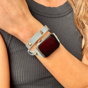 May include: A light blue leather watch strap with gold studs and a gold Apple Watch.