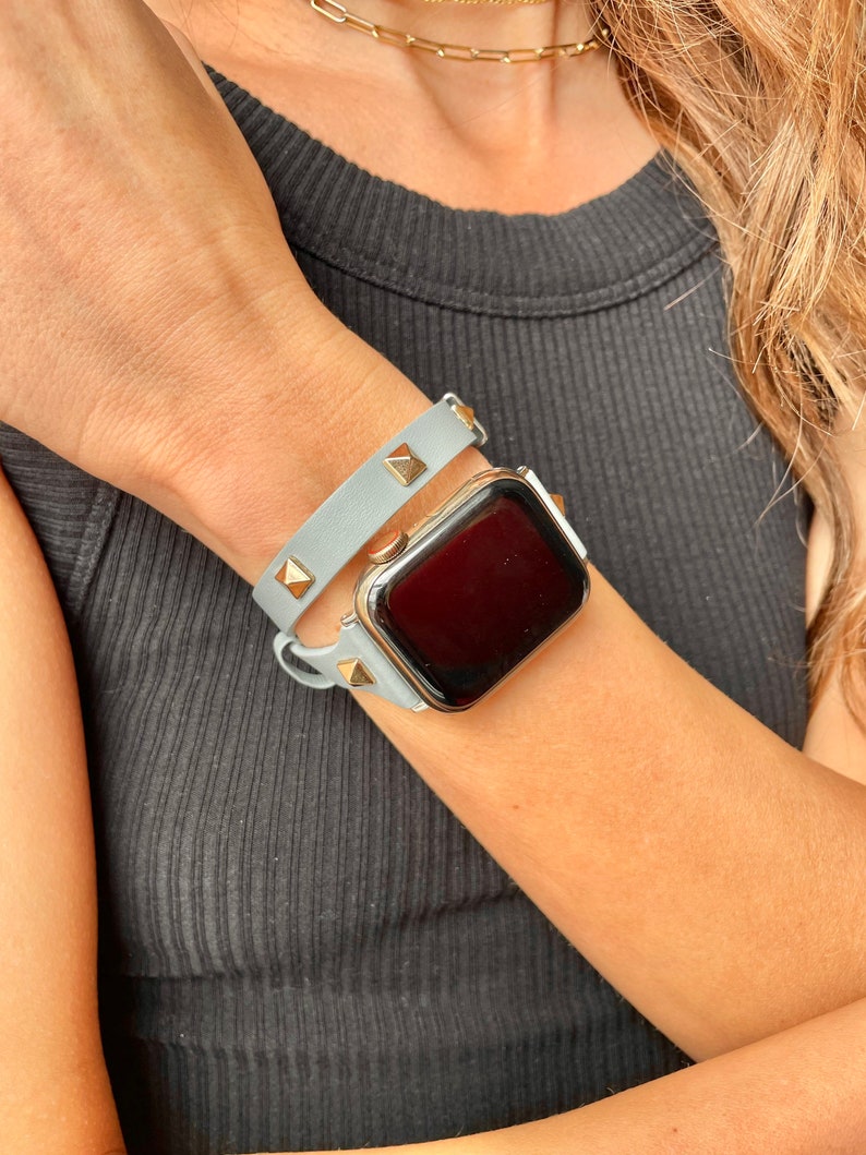 May include: A light blue leather watch strap with gold studs and a gold Apple Watch.