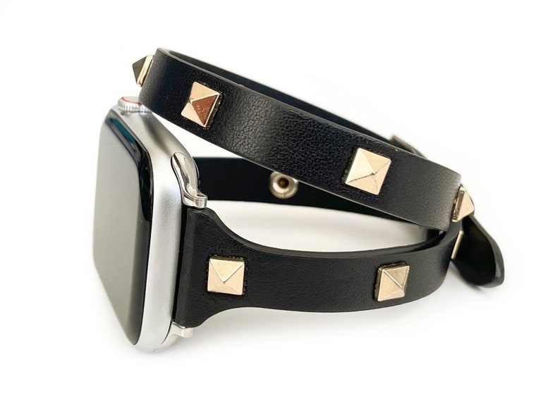 May include: Black leather Apple Watch band with gold pyramid-shaped studs. The band is double-wrapped around the watch.