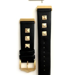 May include: Black leather watch band with gold-tone studs and a gold-tone buckle. The band is shown with two spring bars.